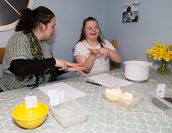 Young woman using Makaton with a girl who has Down's syndrome while baking