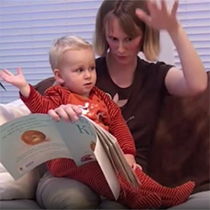 A mother reading and signing to her young son, who is sitting on her lap