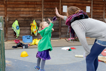 Young girl in playground ;high fiving' with her female teacher