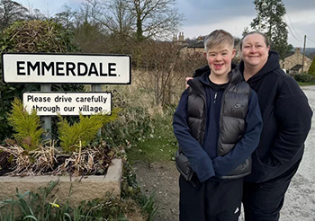 Harvey and Tracy standing next to the Emmerdale sign