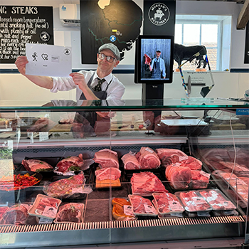 A butcher at his meat counter holding a Makaton symbols board